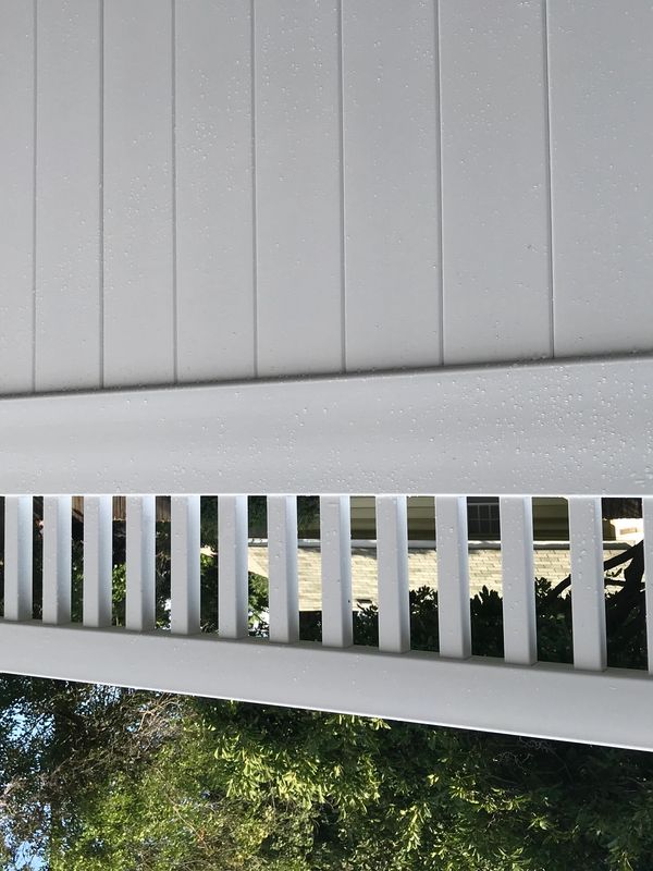 White vinyl fence with vertical slats and trees in the background.