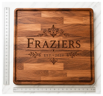 Wooden cutting board engraved with 'FRAZIERS EST. 2024' and decorative designs.