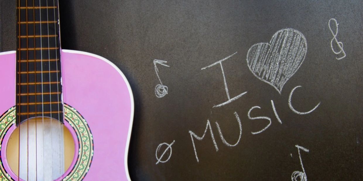 A pink guitar with I love music on a chalk board. 