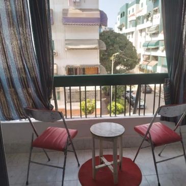 A charming balcony with red cushioned folding chairs, a small white table, striped curtains,