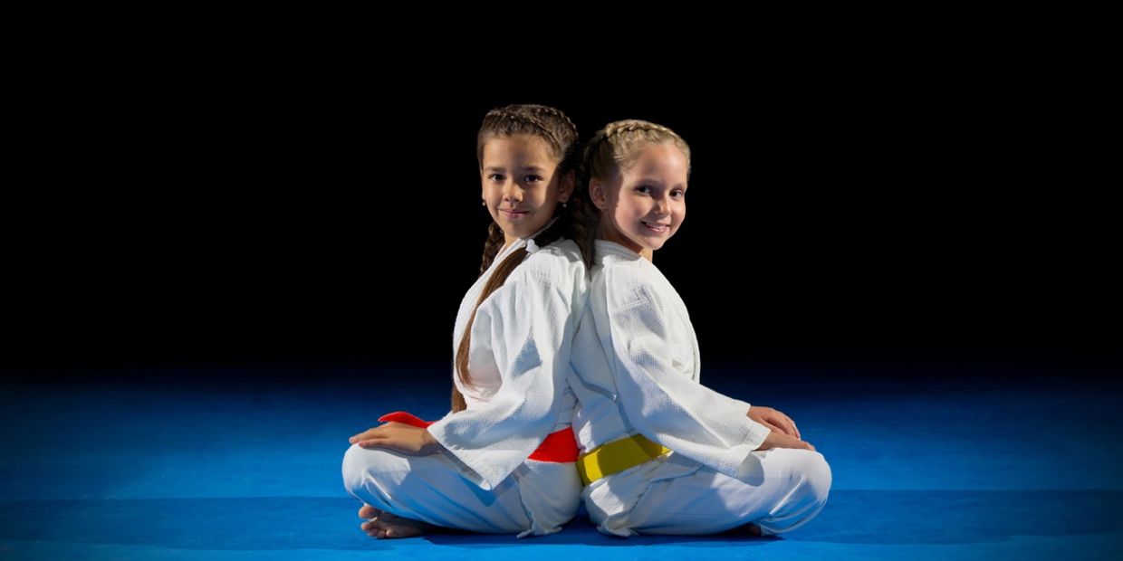 Two young children sitting wearing karate attire
