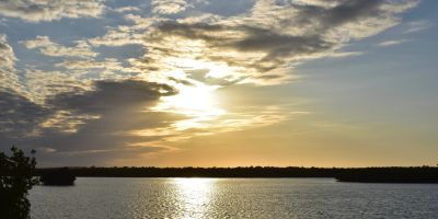 Sun setting over calm water with scattered clouds.