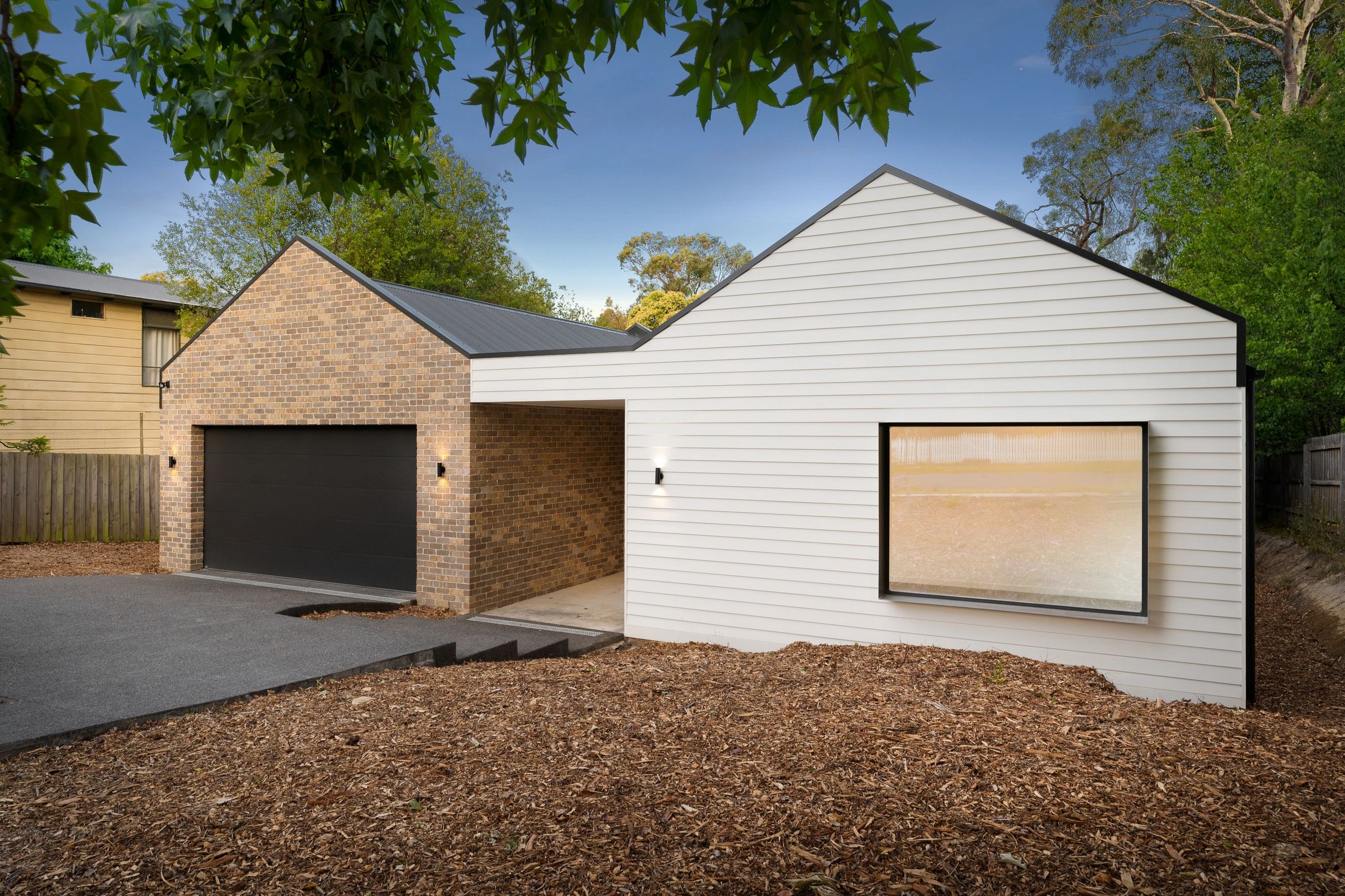 Modern house exterior with brick and white siding, large garage door, and window.