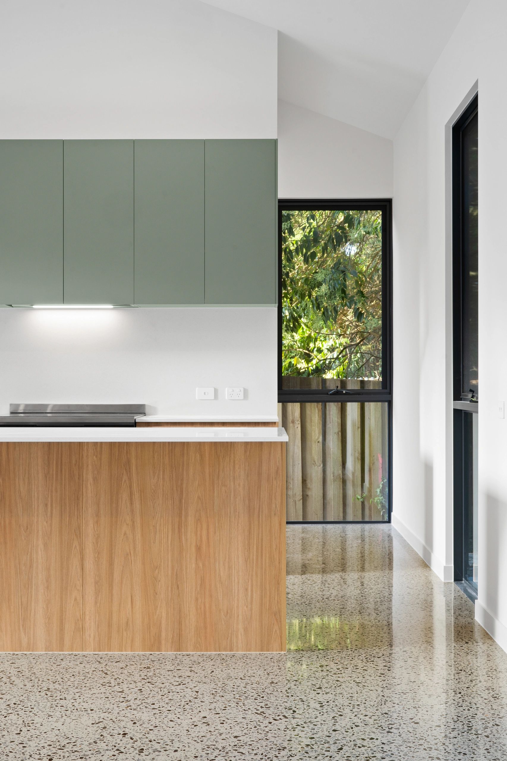 Modern kitchen with green cabinets, wooden island, and polished terrazzo floor.