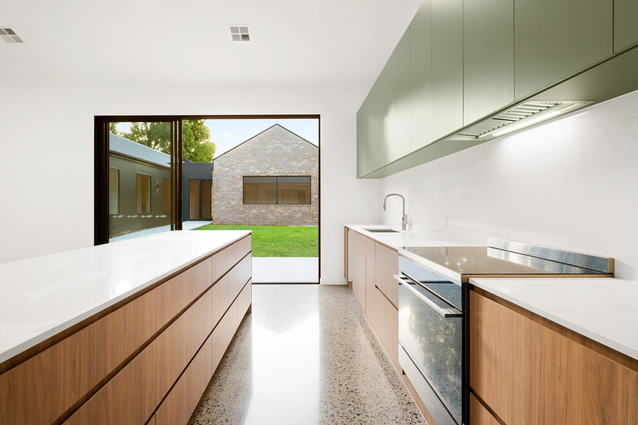 Modern kitchen with wooden cabinets and large window overlooking lawn.