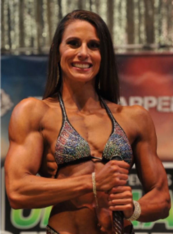 Female bodybuilder smiling on stage during competition.
