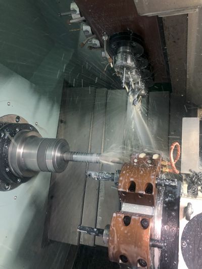 A CNC machine is cutting a metal rod with coolant spraying.