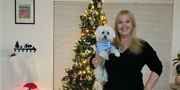 Woman holding a small dog in front of a decorated Christmas tree.