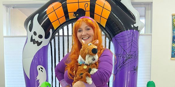 Woman in purple costume holding a Scooby-Doo dog plush.