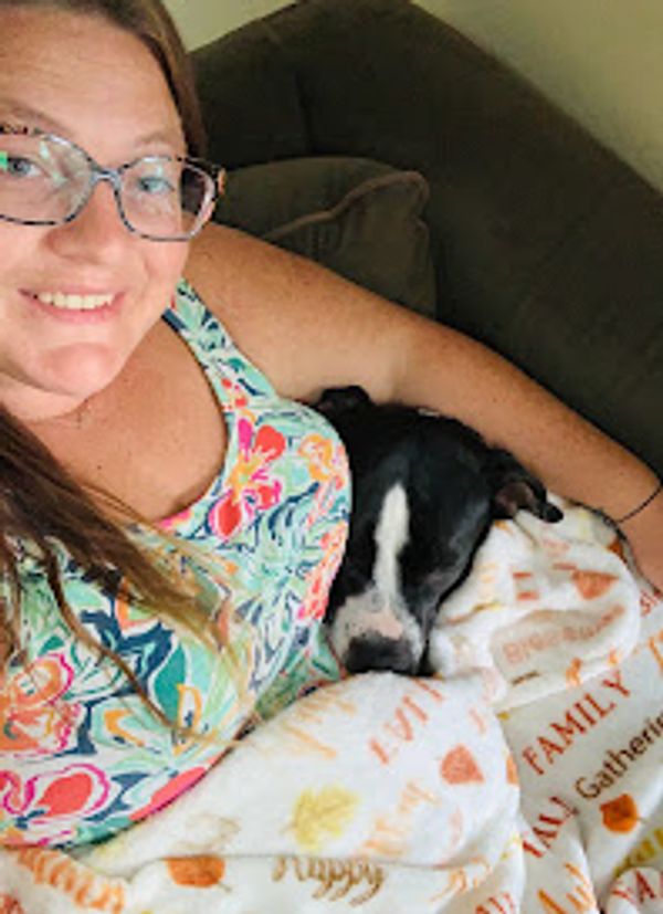 Woman smiling with dog wrapped in blanket.