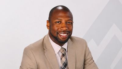 Smiling man in a beige suit and plaid tie.