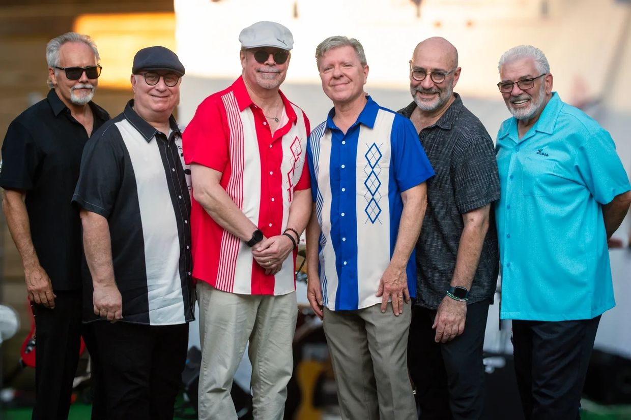 Six men posing together, wearing casual shirts and smiling.