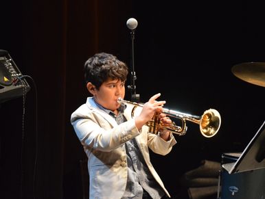 A young boy passionately playing a trumpet on stage.
