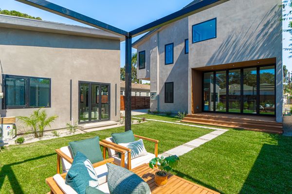 Modern backyard with stylish patio furniture and green lawn between two contemporary houses.