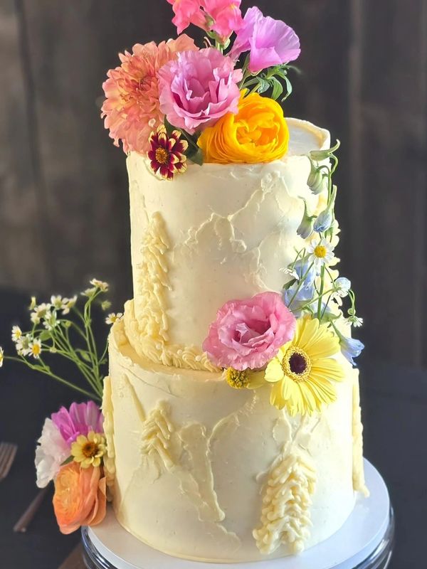Two-tiered cream cake decorated with colorful fresh flowers.