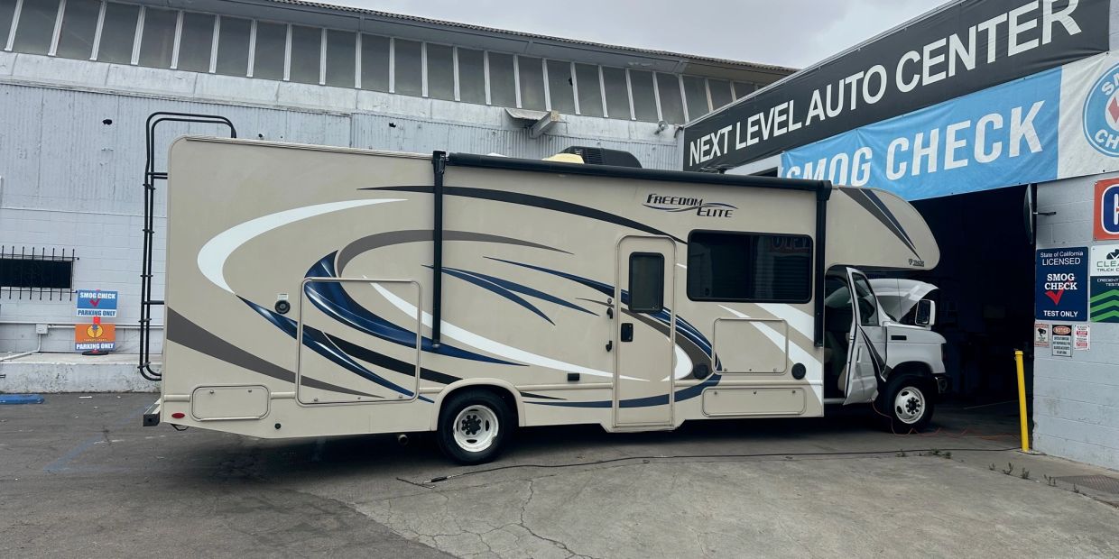 A beige Freedom Elite RV parked outside a smog check auto center.