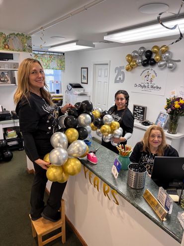 Staff smiling and decorating with balloons to celebrate 25th anniversary.