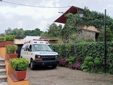 An ambulance parked near a lush garden and stone building.