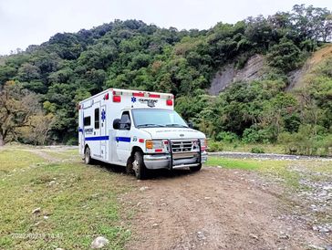 An ambulance parked on a dirt path near a forested hill.