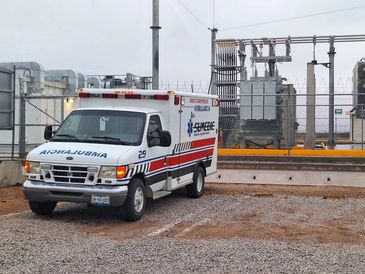 Ambulance parked outside an industrial facility on a gravel surface.