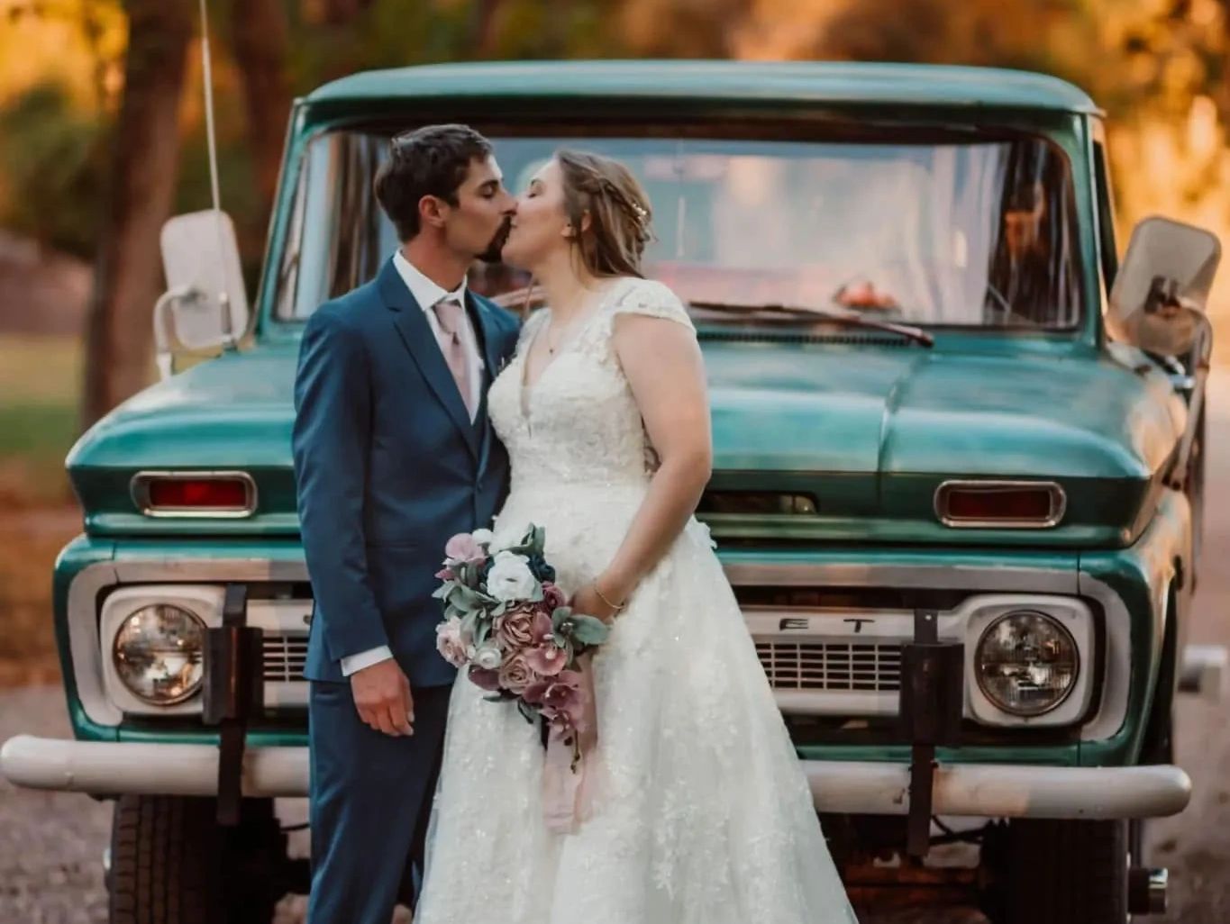 Newlywed couple sharing a kiss in front of a vintage green truck.