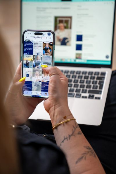 Person scrolling social media on phone with laptop in background.