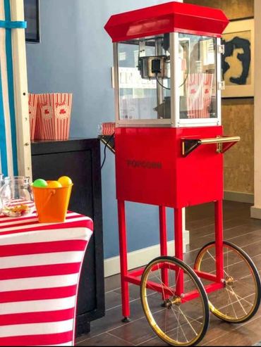 Vintage-style red popcorn machine on wheels beside a striped table.