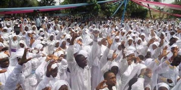 Large crowd dressed in white at an outdoor event raising their hands.