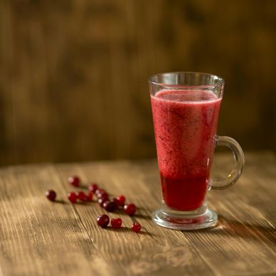 A glass of red berry smoothie on a wooden table with scattered berries.