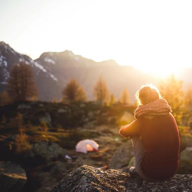 Person sitting on a rock watching the sunset in a mountainous area.