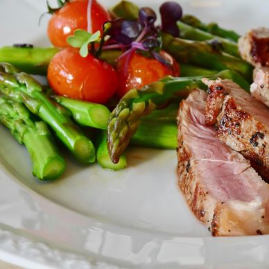 Grilled steak with asparagus and cherry tomatoes on a white plate.