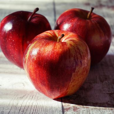 Three shiny red apples on a wooden surface.