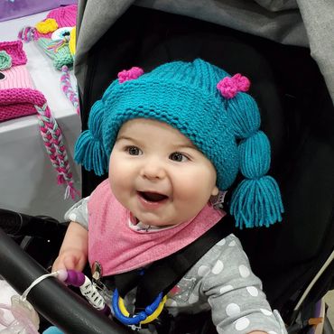 Happy baby in a blue knitted hat and pink bib.