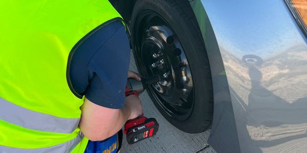 Person in a yellow vest changing a car tire with a power tool.