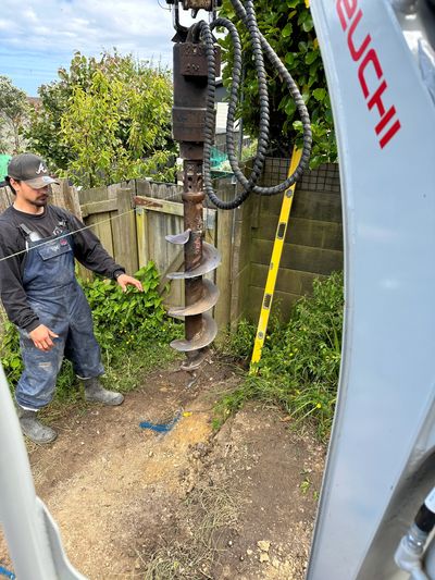 Worker operates a large drill for digging in a residential backyard.