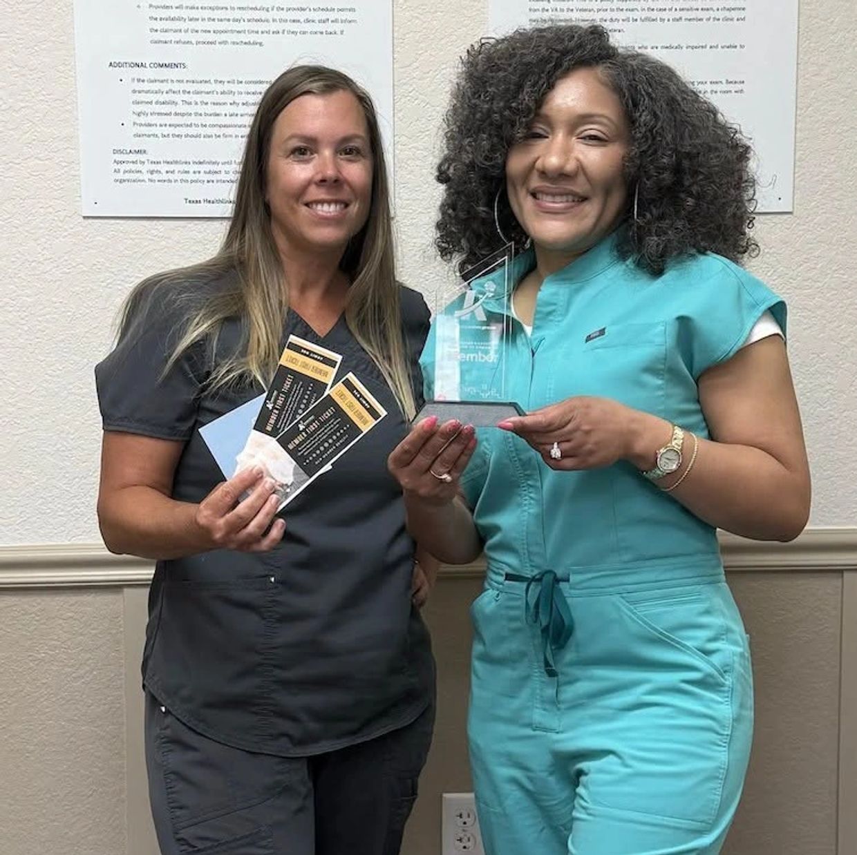 Two smiling women in scrubs holding an award and tickets.