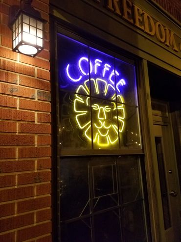 Neon coffee sign with lion face on a window at night.