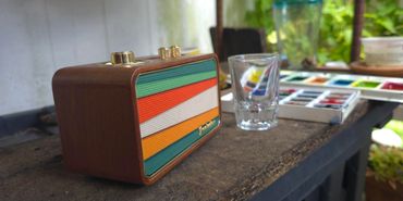 Retro radio with a glass and watercolor palette on a rustic table.