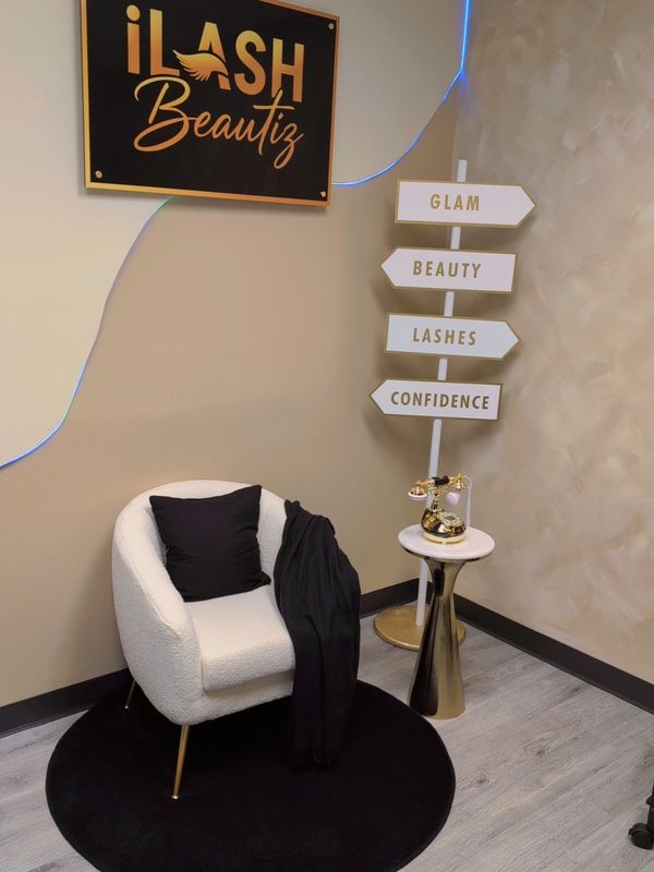 Chic waiting area with white armchair, black pillow, gold accents, and beauty-themed signs.