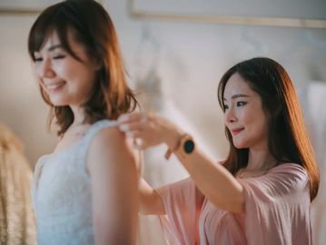Woman helping another woman with dress fitting.