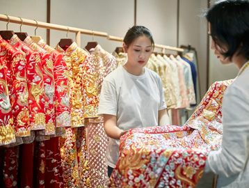 Women inspecting traditional embroidered dresses in a store.