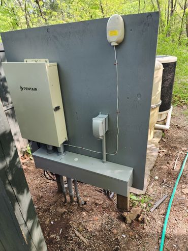 Outdoor electrical control panel and wiring setup by Pentair next to a pool filter.