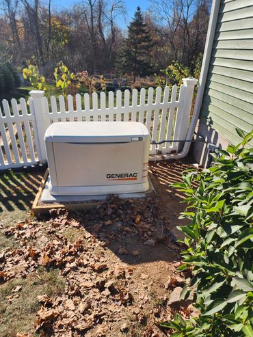 A Generac generator installed beside a house with a white picket fence.