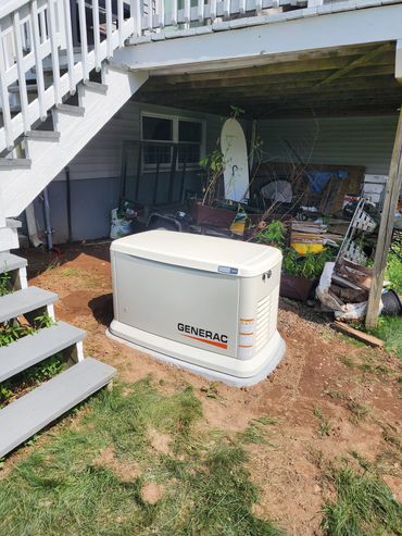 Generac backup generator installed outside under a deck near stairs.