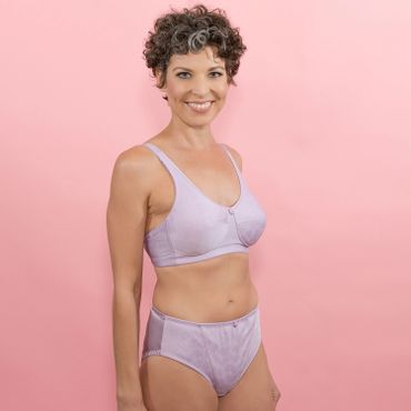 Smiling woman in lavender lingerie against a pink background.