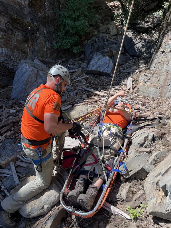 Rescue team assists an injured person on a stretcher in a rocky outdoor area.