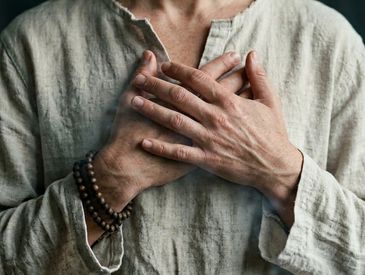 Person with hands crossed on chest wearing a linen shirt and beaded bracelet.