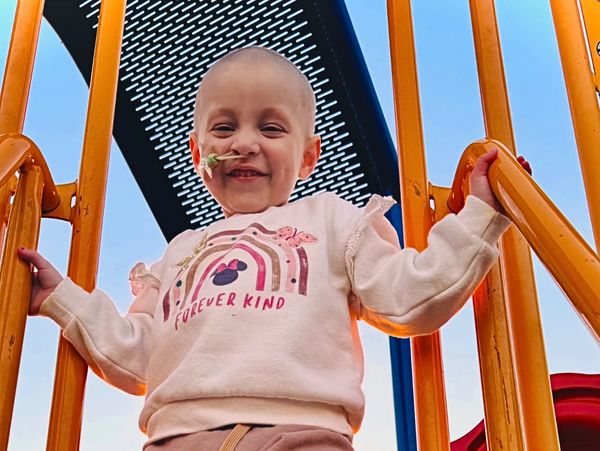 Smiling child standing on playground stairs during sunset.