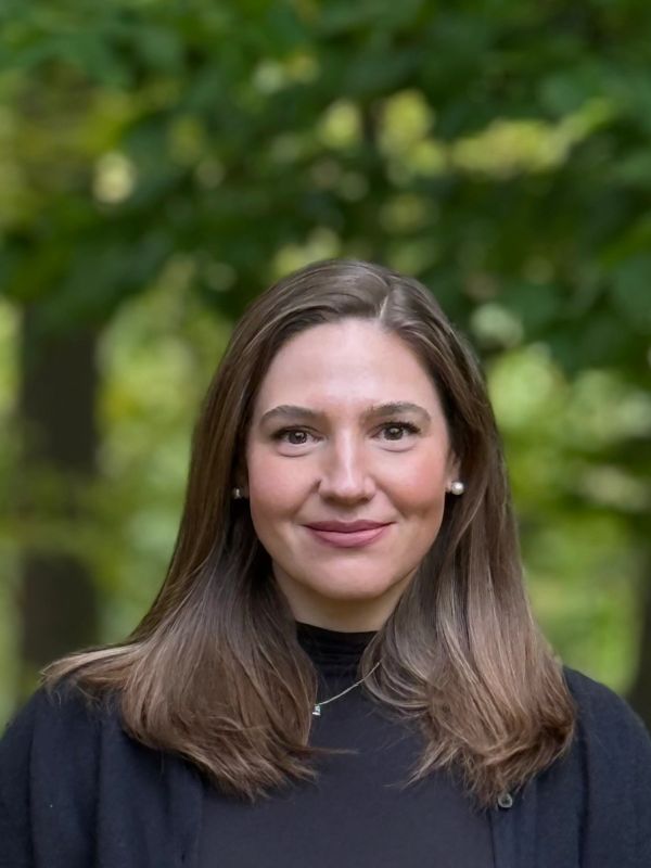 Smiling woman with brown hair outdoors.