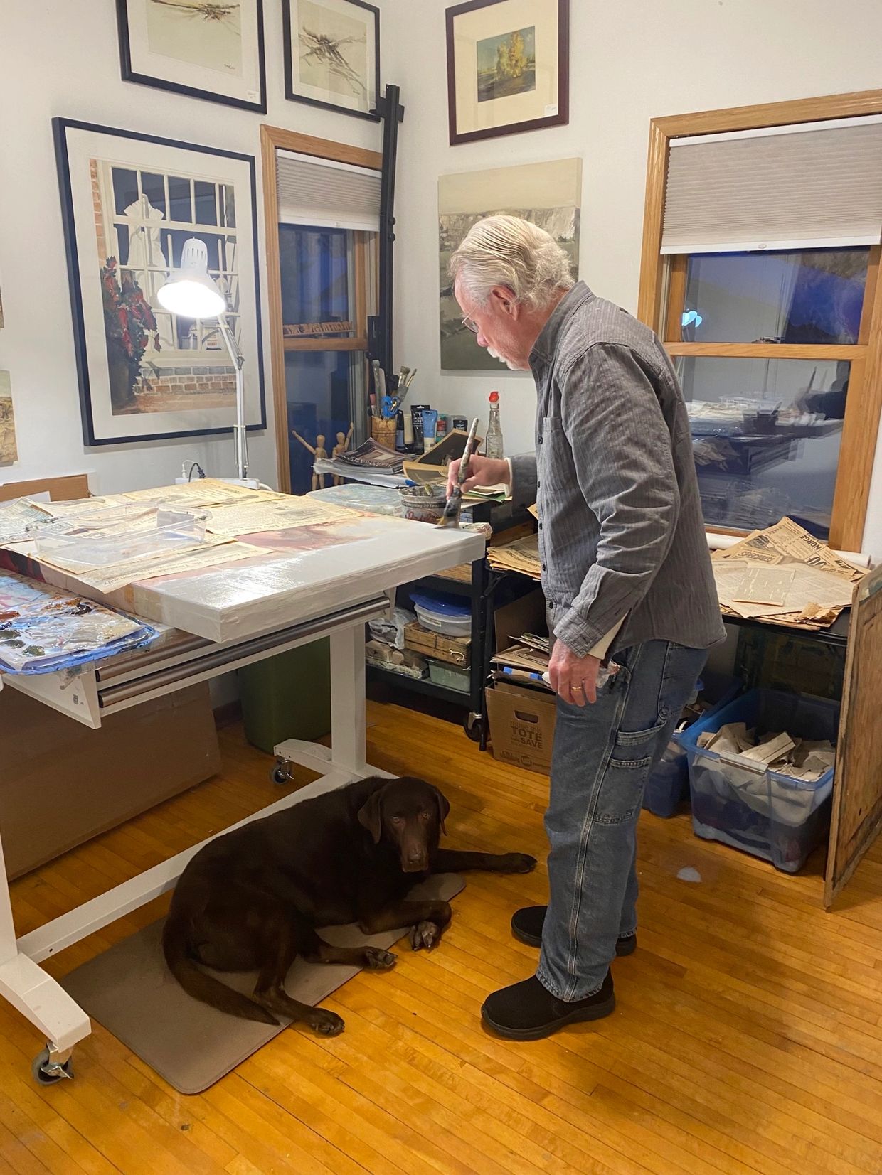 An artist painting in a studio with a dog lying on the floor.